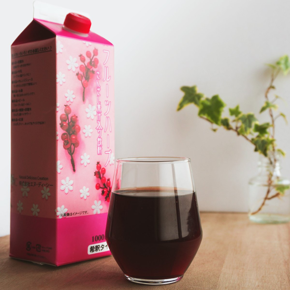 木目テーブルの上に置かれたさんざしドリンクの紙パックとグラスに注がれた赤い飲料